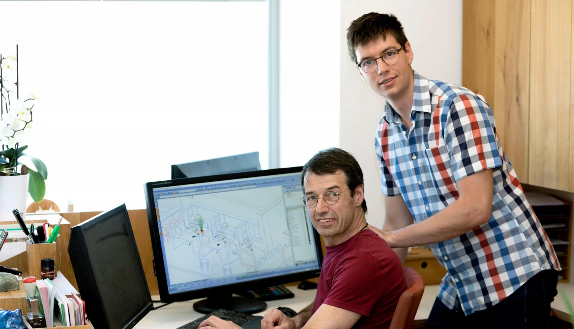 Tischlermeister Max Schlemaier und Sohn und Geschäftsführer Markus gemeinsam in einem Büro während sie an einem Computer arbeiten.